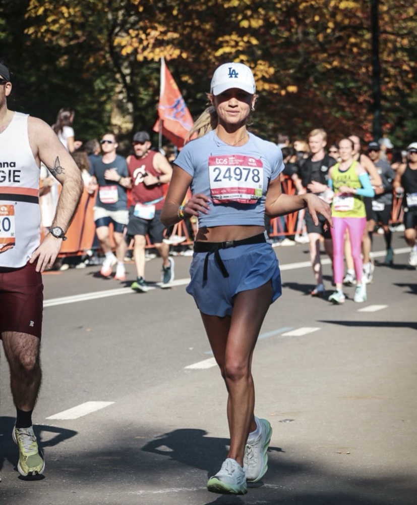 Nikki Kay running a marathon in a blue crop top and Dodgers cap