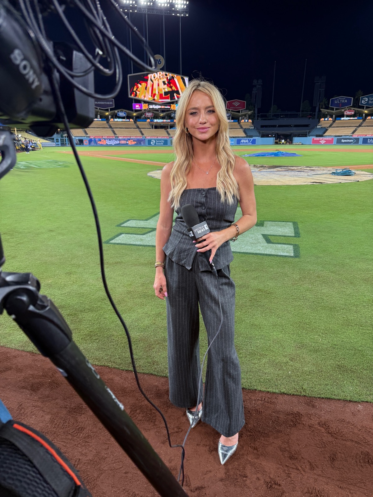 Nikki Kay reporting live from the field at Dodger Stadium with a Spectrum News 1 microphone